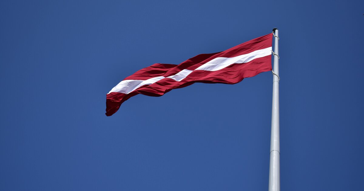Latvijas karogs — karmīnsarkans ar baltu joslu — zilās debesīs.